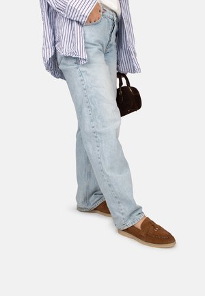 Jeans de mezclilla azul claro con un corte relajado, combinados con mocasines de gamuza marrón. Una camisa de rayas claras completa el conjunto.