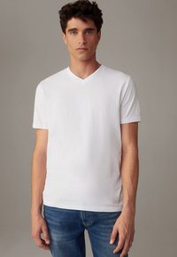 Weißes Baumwoll-T-Shirt mit kurzen Ärmeln, subtilen V-Ausschnitt, glatter Textur und figurbetontem Schnitt, kombiniert mit blauen Jeans.