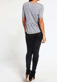 Top gris de manga corta con lunares negros, cintura peplum, combinado con jeans skinny negros y botas de tacón alto negras hasta el tobillo.