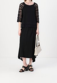 Abito nero con maniche in pizzo e gonna a strati. Abbinato a sandali neri con tacco a blocco e una borsa a tracolla grigia chiara.