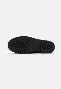 Suela de zapato de goma negra con un patrón de tracción profundo, que presenta diseños de estrellas y acentos texturizados. Superficie plana con un área de logo rectangular.
