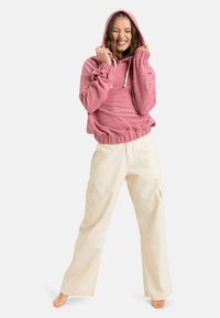 Pink hooded sweatshirt with a textured fabric, drawstrings, and relaxed fit, paired with wide-leg cream cargo pants featuring side pockets.