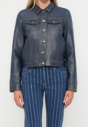 Kvinde iført en mørk sortvasket denimjakke med knaplukning og højttaljede blå jeans med lodrette hvide striber.