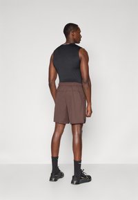 Black sleeveless top with a rounded neckline, paired with brown shorts featuring an elastic waistband, set against a neutral background.