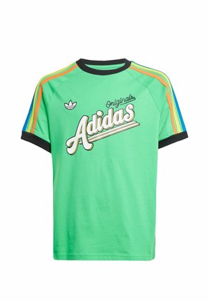 Dwóch chłopców stoi obok siebie, ubranych w zielone koszulki Adidas z kolorowymi paskami i casualowe spodnie, patrząc pewnie w kamerę.