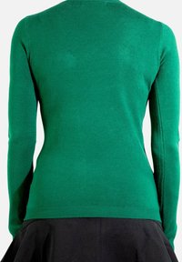 Pull à manches longues vert avec une texture lisse, un design ajusté, un ourlet côtelé et des épaules sans coutures, associé à une jupe noire.