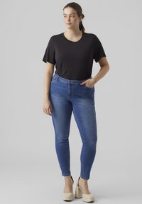 Black short-sleeve shirt and blue skinny jeans with a high waist. Light-colored platform shoes with a black accent. Smooth denim texture.