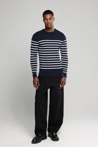 Marine-stribet sweatshirt med hvide striber, rund hals og ribbede manchetter; parret med brede sorte bukser og sorte sko. Enkel design.