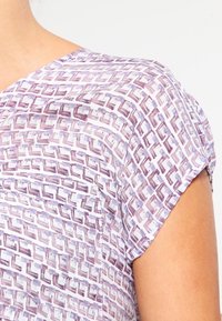 Kortärmad blus med ett geometriskt mönster i lila och vitt. Lättviktig tyg med mjuk textur och en avslappnad passform.