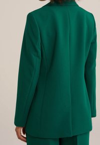 Grön blazer med skräddarsydd passform, spettslaget krage och strukturerade axlar. Har en enda bakslits och slät yta.