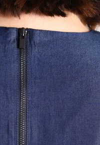 Meriini sininen kangas hienovaraisella kiillolla, jossa on musta vetoketju takana. Tekstuuuri on sileä, ja siinä on hieno, tasainen kudonta.