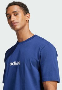 Tamsiai mėlyna medvilnė t-shirt su trumpomis rankovėmis ir apvaliu kaklu, priekyje su spausdintu baltu "adidas" logotipu. Sklandi tekstūra.