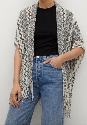 Femme portant un t-shirt noir à manches courtes, un jean bleu taille haute et un châle à franges noir et blanc à motifs sur les épaules.