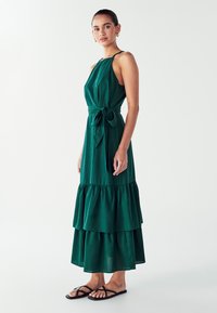 Grünes, gestuftes Maxikleid mit Halterneck und Taillenknot. Hergestellt aus einem leichten Stoff; verfügt über fließende Lagen und eine lockere Passform.