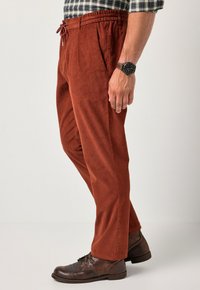 Ruskosuoran corduroypantit, joissa on joustava vyötärö ja nyöri. Sileä pinta, suora leikkaus, yhdistetty tummanruskeisiin nauhatoimisiin saappaisiin.