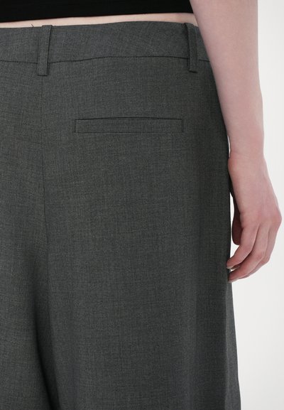 Pantalons gris sur mesure avec une texture subtile, dotés d'une taille plate et d'une poche arrière. Jambes droites ourlées et design minimaliste.
