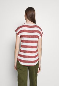 Camiseta de mangas cortas a rayas rojas y blancas con dobladillo redondeado y un acabado texturizado, mostrada en una persona de espaldas al espectador.