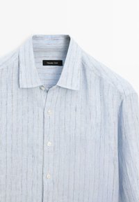 Camicia azzurra chiara a righe con bottone frontale e colletto morbido, etichettata "Massimo Dutti." Esibita piatta su uno sfondo bianco.