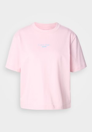 T-shirt di cotone rosa con scollo rotondo, maniche corte e logo blu "Calvin Klein JEANS" posizionato centralmente sul petto.