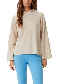 Maglione beige con cappuccio in texture a costine, caratterizzato da una vestibilità ampia e maniche larghe. Abbinato a pantaloni aderenti blu chiaro.