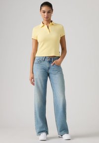 Κίτρινο ριμπ πουκάμισο πόλο με γιακά, συνδυασμένο με ανοιχτό μπλε παντελόνι φαρδιάς γραμμής και λευκά αθλητικά παπούτσια. Απλή και καθημερινή εμφάνιση.