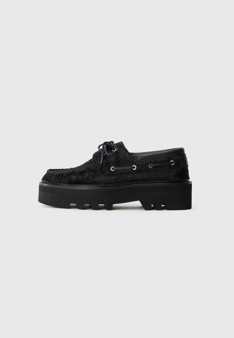 Zwarte schoenen met een stevige plateauzool en een textuur van bont. Voorzien van ronde veters, gouden oogjes en een gestructureerde rubberen zool.