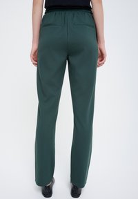 Zielone dresowe spodnie z elastycznym paskiem w wąskim kroju, z dwoma tylnymi kieszeniami i zwężanymi nogawkami, wykonane z miękkiego, gładkiego materiału.