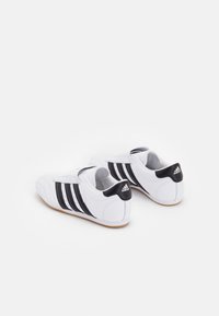 Vita idrottsskor i vitt med svarta ränder och accenter. Tillverkade av läderliknande material med vadderad krage och kardborreband. Gummisula.