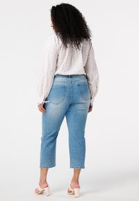 Jean bleu court avec des détails embellis et une taille haute. Associé à un blouse de couleur claire avec un motif subtil.