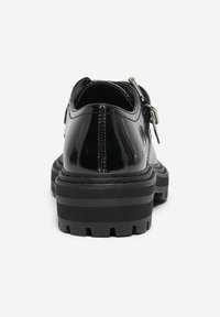 Chaussures en cuir noir avec une finition brillante, présentant une semelle épaisse et texturée ainsi qu'un détail de boucle sur le côté. Vue arrière montrant les coutures.