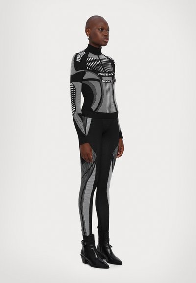 Enges schwarz-graues Sportanzug-Set mit geometrischen Mustern, hohem Kragen und gemusterten Akzenten. Kombiniert mit schwarzen Absatz-Stiefeletten.