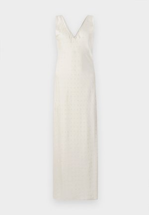 Duga haljina boje kreme s V-izrezom i tankim naramenicama. Tkanina je glatka s suptilnim dekorativnim perforacijama po cijeloj površini.