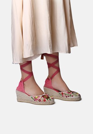 Roza vezeni espadrilni klinasti čevlji z pletenimi jutnimi podplati in prekrižanimi trakovi okoli gležnja. Cvetlični vzorci krasijo sprednji del. Mehak občutek.