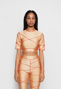 Conjunto de duas peças com um top curto de mangas curtas e leggings de cintura alta. Feito de um tecido beige liso e brilhante, com costuras vermelhas em contraste.