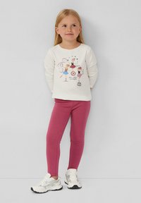Camicia bianca a maniche lunghe con grafiche colorate di balletto; abbinata a leggins rosa e sneakers bianche con accenti grigi.