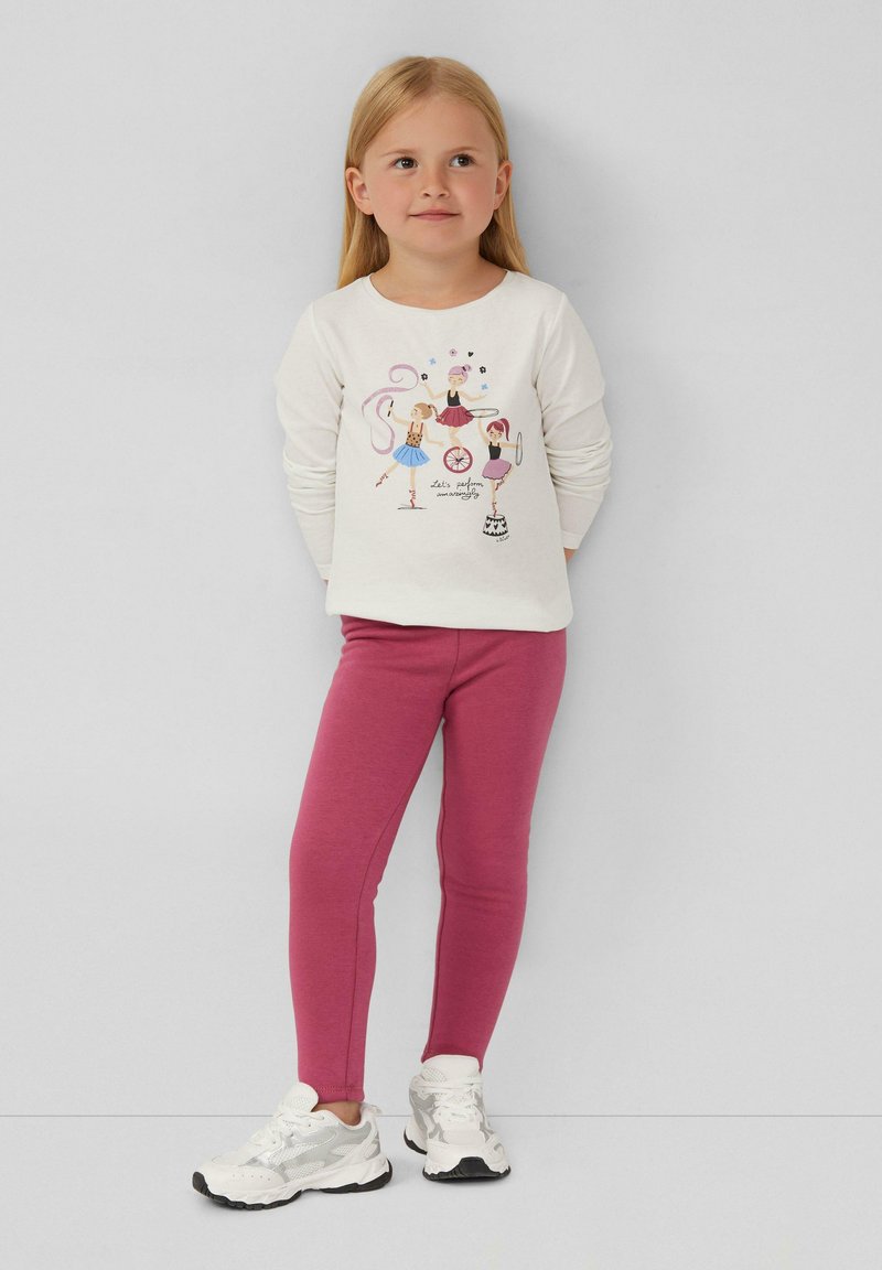 Camicia bianca a maniche lunghe con grafiche colorate di balletto; abbinata a leggins rosa e sneakers bianche con accenti grigi.