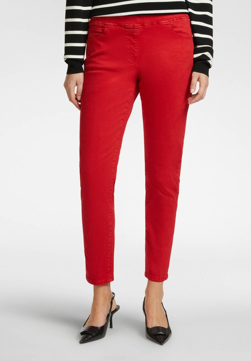Pantalones rojos ajustados de algodón, con una textura suave y diseño de cinco bolsillos. Combinados con unos zapatos de tacón alto negros y una blusa a rayas.