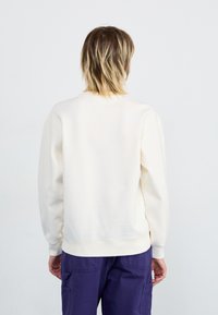 Cremefarvet sweatshirt med rund hals, ribbede ærmer og kant. Materialet ser blødt og glat ud. Bæres med lilla cargo-bukser.