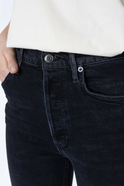 Zwarte denim jeans met een slim fit ontwerp, voorzien van een metalen knoopsluiting en frontzakken. De textuur lijkt licht beschadigd.