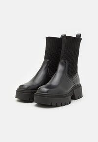 Botine negre din piele cu un superior din tricot texturat, talpă din cauciuc chunky și bucată pentru a fi ușor de încălțat. Prezintă un design modern și elegant.