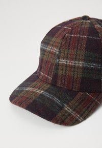 Casquette de baseball en tissu de laine à carreaux marron, vert et rouge, avec une visière courbée et un bouton sur le dessus, le tout sur un fond blanc.