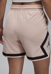 Pantalones cortos deportivos de color rosa claro hechos de tela texturizada con una cintura elástica, con detalles en negro y un logo de Jumpman.
