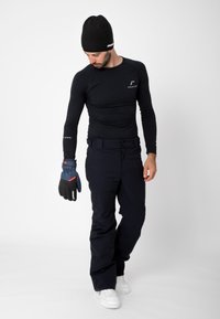 Svart långärmad topp, marinblå byxor, stickad svart mössa och blå handskar med röda detaljer. Vita sneakers fulländar outfiten.