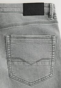 Szürke farmernadrág hátsó zsebbel, amely hegyes varrási részlettel rendelkezik, fekete bőrbegyűjtővel a derékrészen, valamint finom texturált anyaggal.