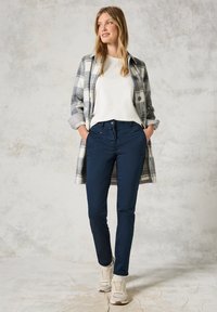 Grå och vit rutig kappa över en vit topp, tillsammans med marinblå byxor och beige sneakers. Tyget verkar mjukt med en avslappnad passform.