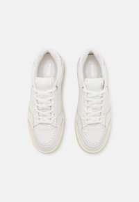 Balti sportiniai batai su tekstūruota odine viršutine dalimi, apvaliu pirštu, raišteliais priekyje ir perforuotais akcentais. Šviesios spalvos gumos padas.