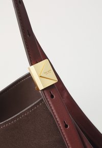 Cintura in suede e pelle marrone scuro con fibbia quadrata dorata incisa "kate spade new york" su sfondo bianco.