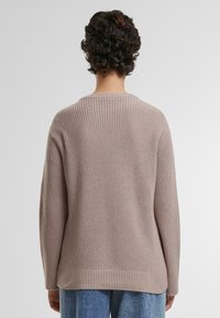 Lyserød strikket sweater med ribbet tekstur, rund halsudskæring og sænkede ærmer. Bagsiden har en lige kant.