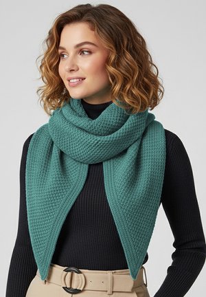 Ein strukturiertes, petrolfarbenes Halstuch, umwickelt und drapiert, mit einem gewebten Muster und leichtem Glanz, kombiniert mit einem schwarzen Rollkragenpullover und einem beigen Gürtel.