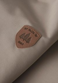 Beige stof med en glat tekstur har en brun læderpatch prydet med træer og koordinater, hvilket forbedrer designets naturlige tema.